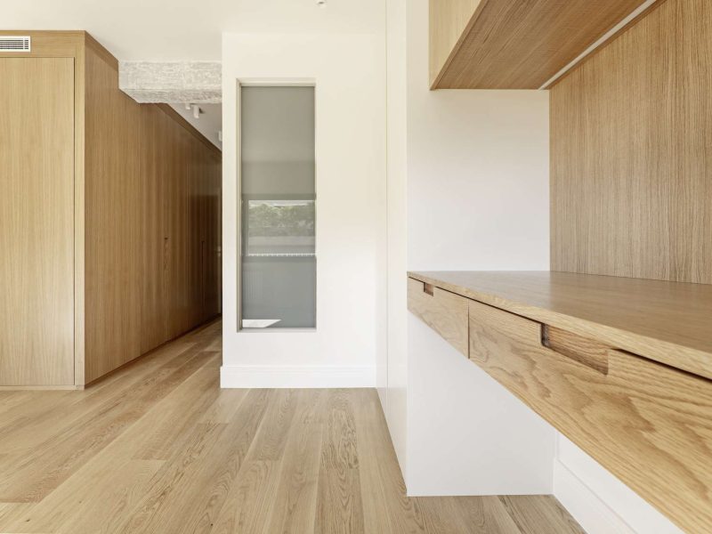 Contemporary designed bedroom with custom oak door closet, skylight leading to ensuite bathroom, raw concrete beams, wall-mounted desk